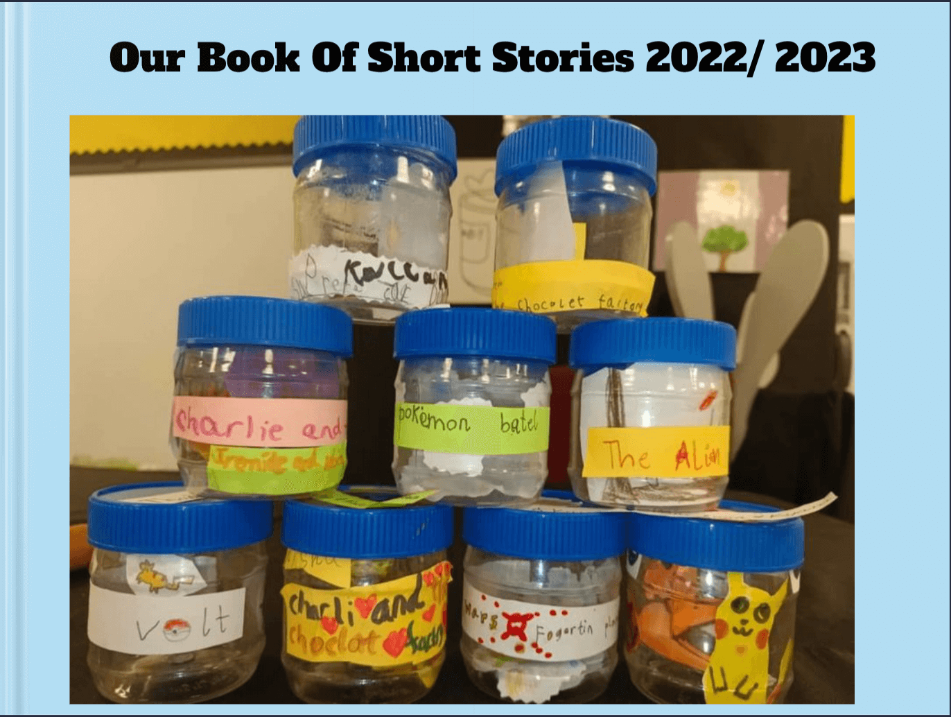 A light blue book cover featuring a classroom project with stacked plastic jars, each labeled with handwritten story titles and decorated with colorful stickers, including Pokémon and other child-friendly themes. The title reads "Our Book Of Short Stories 2022/2023.
